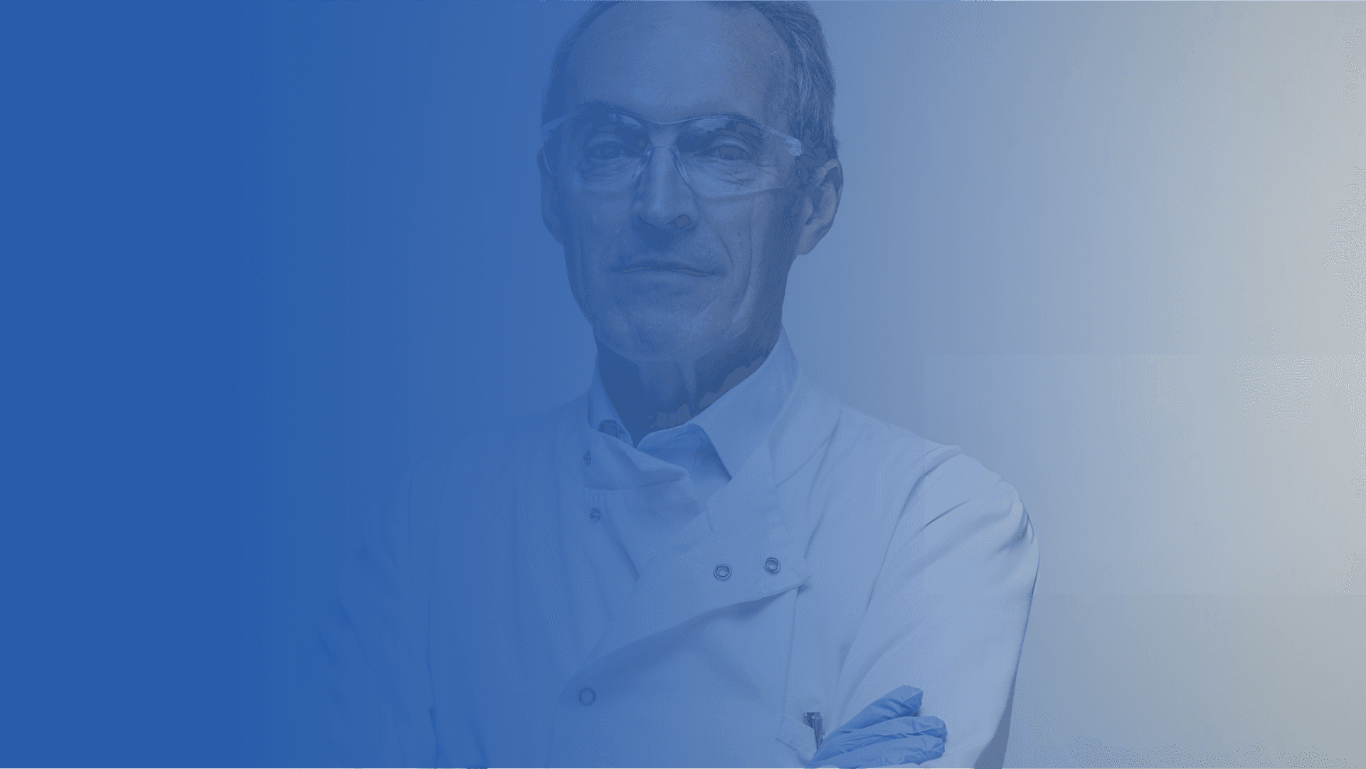 A mature male scientist or doctor wearing safety glasses and a white lab coat.